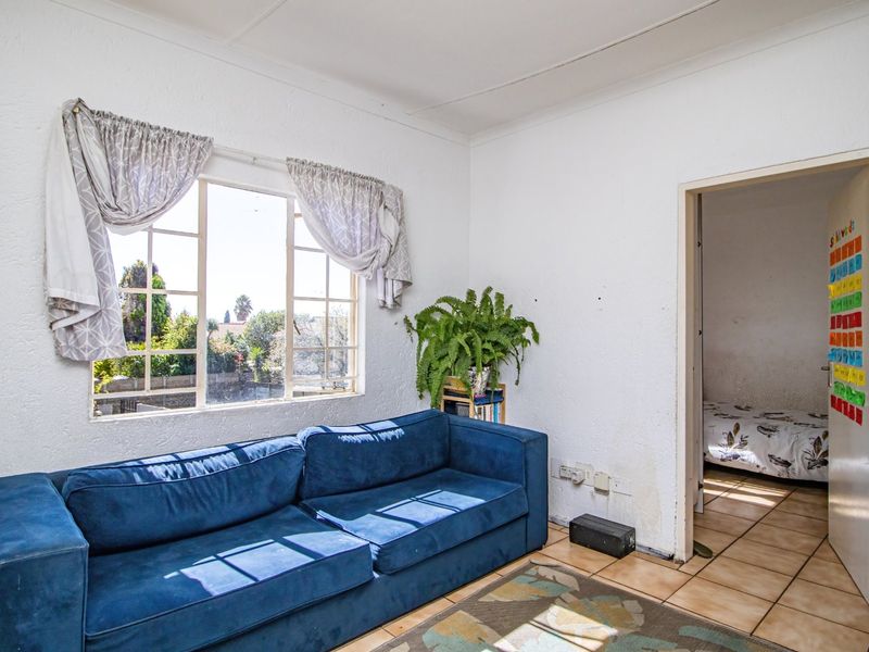 A living room featuring tiled flooring and a steel-framed window, showing signs of wear and wall damage requiring maintenance.