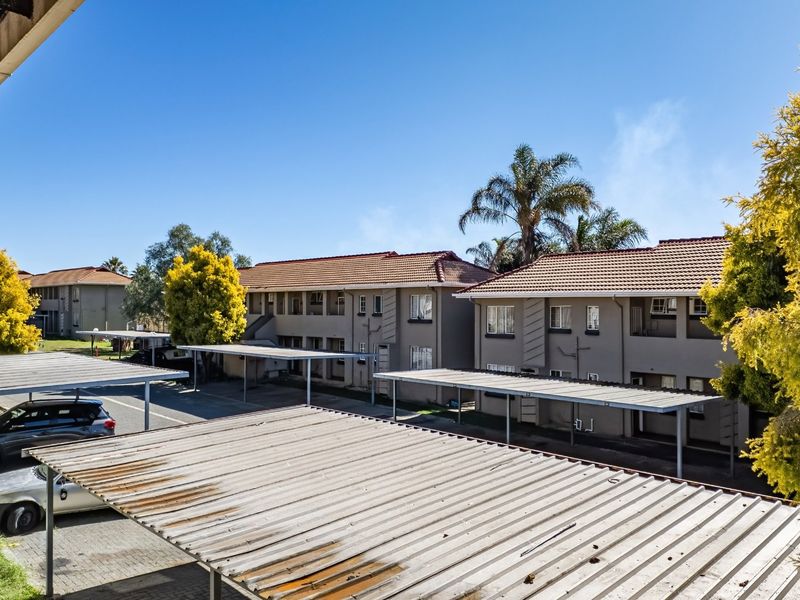 Exterior view of the townhouse complex featuring multiple covered parking bays with tiled roofing and paved driveway access.