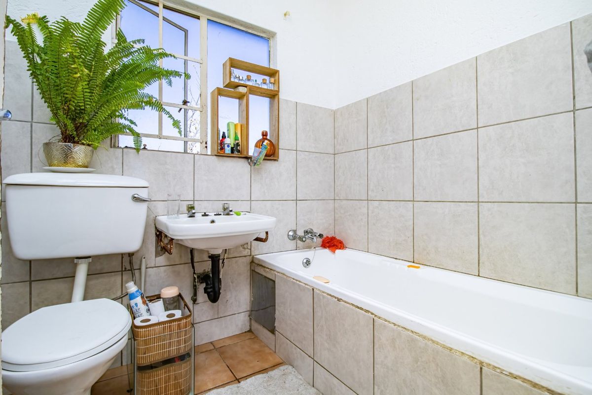 A dated bathroom featuring a standard bathtub, pedestal washbasin, and toilet with neutral wall tiling and a steel-framed window.