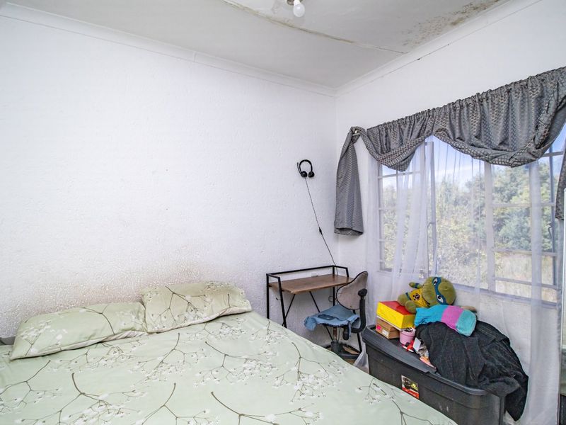 A bedroom featuring a window with curtains and visible signs of ceiling and wall surface deterioration requiring maintenance.