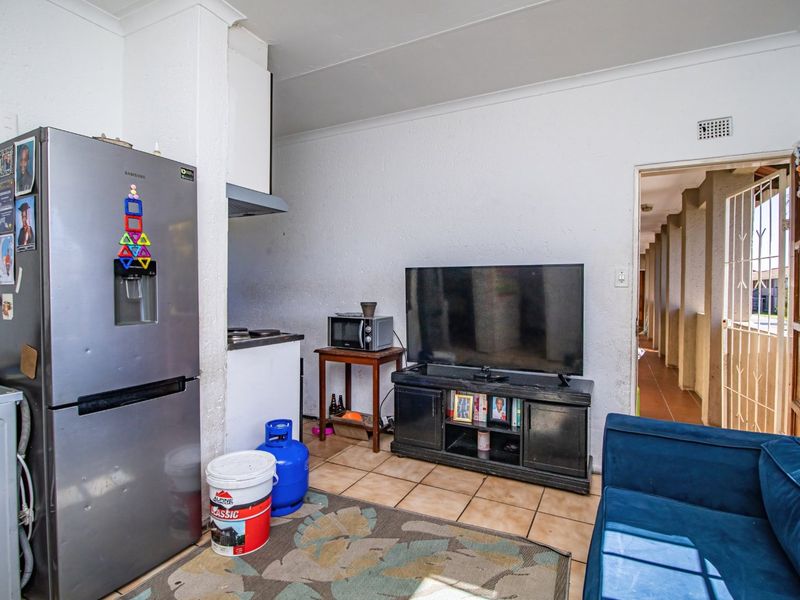 Open plan living area featuring tiled flooring and a compact kitchen corner with an extractor fan and hob, leading to a hallway.
