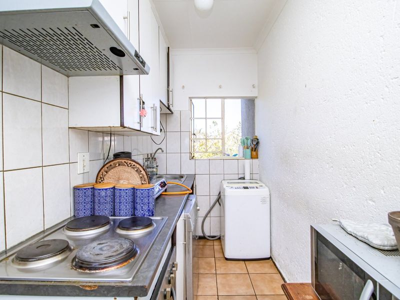 Compact kitchen featuring built-in cabinetry, electric hob with extractor fan, tiled splashback, and dedicated space for laundry appliances.