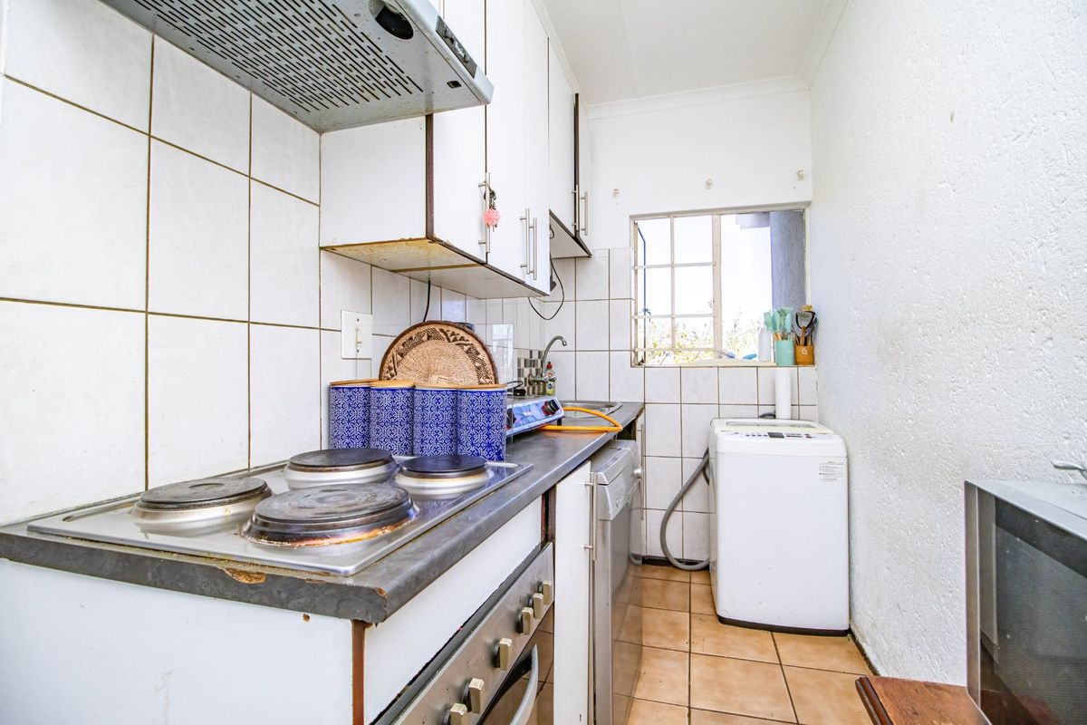 Compact kitchen featuring a built-in electric hob, oven, extractor fan, and tiled splashback with functional cabinetry and tiled flooring.