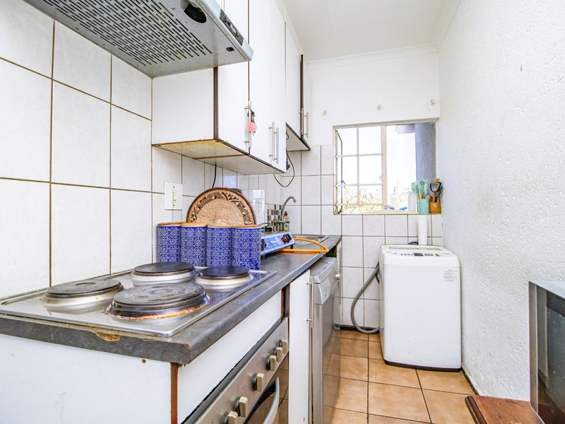 Compact kitchen featuring a built-in electric hob, oven, extractor fan, and tiled splashback with functional cabinetry and tiled flooring.