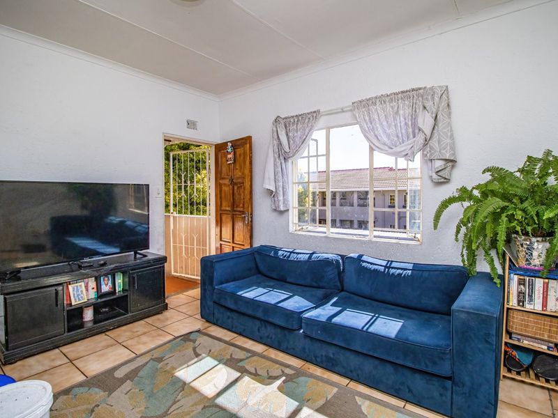 A living room featuring tiled flooring, a security gate, and a window with security bars, offering a functional space with potential for modernization.