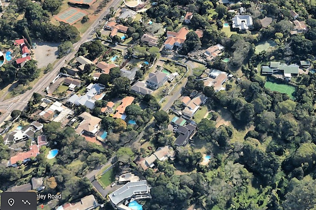 An aerial view of a residential neighborhood featuring established trees, various properties, and surrounding infrastructure.