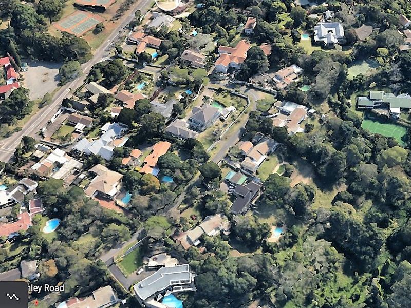 An aerial view of a residential neighborhood featuring established trees, various properties, and surrounding infrastructure.
