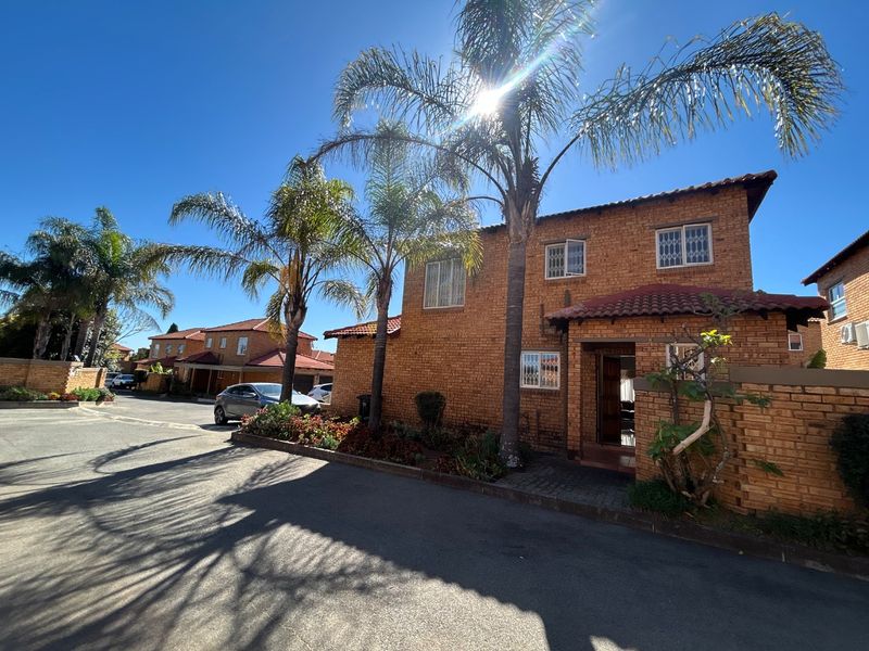 A well-maintained double-story face brick townhouse featuring a tiled roof, security window bars, and a neat front garden area.