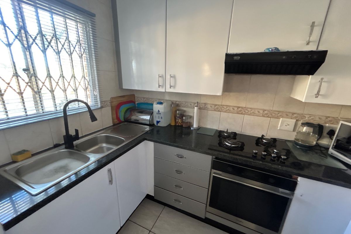 A functional kitchen featuring granite countertops, a double sink with a modern mixer tap, built-in oven, gas hob, and white cabinetry.