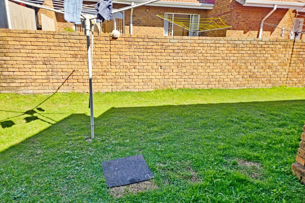 A private rear garden area featuring a brick boundary wall and a grass lawn, viewed from the back of the townhouse.