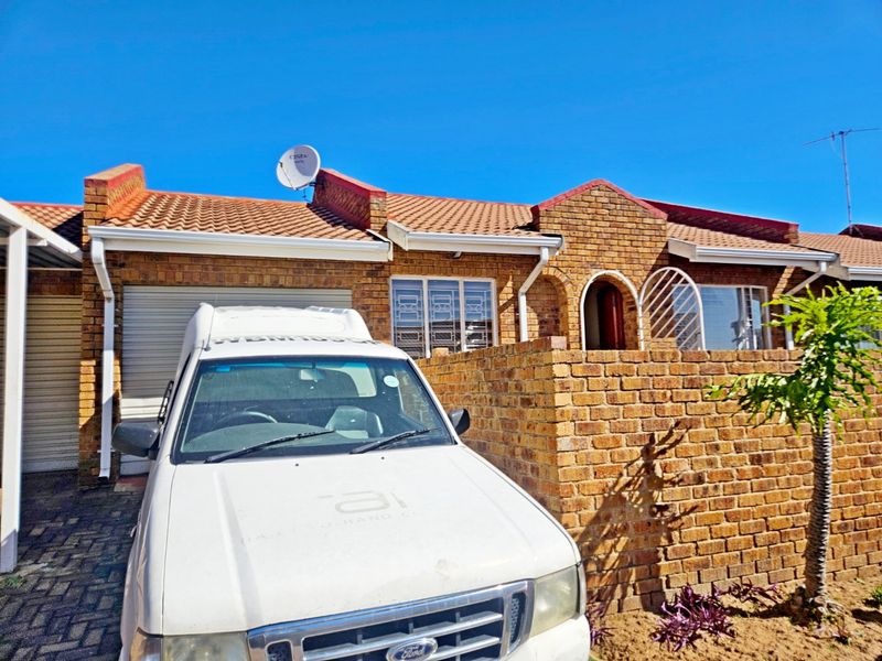 Front elevation of a face brick townhouse featuring a tiled roof, garage access, and a secure entrance gate.