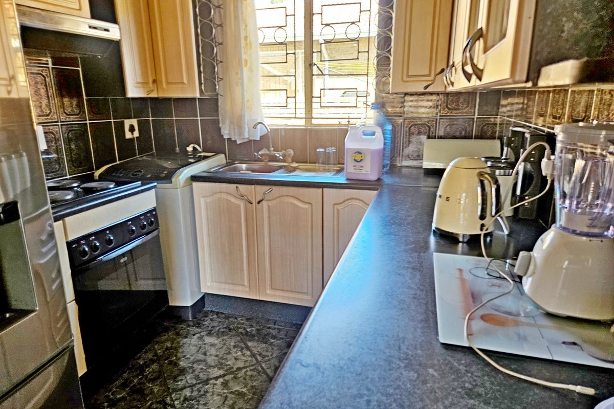 A functional kitchen featuring built-in cabinetry, dark laminate countertops, a tiled backsplash, and a freestanding stove with an extractor fan.