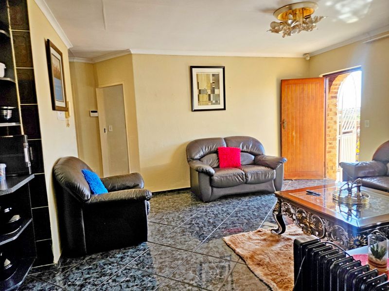 A living room featuring dark patterned floor tiles, neutral wall finishes, and a timber entrance door leading to an outdoor area.
