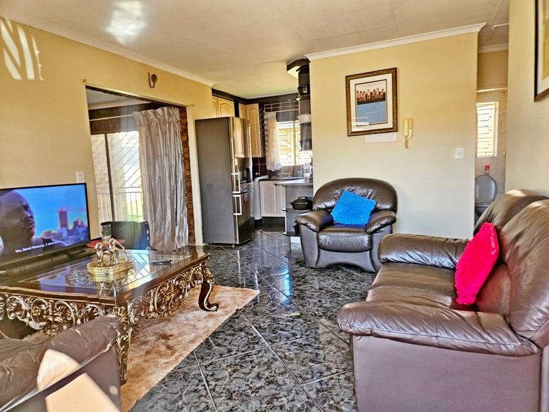 Open plan living area featuring dark tiled flooring, coved ceilings, and a view through to the kitchen and rear patio area.