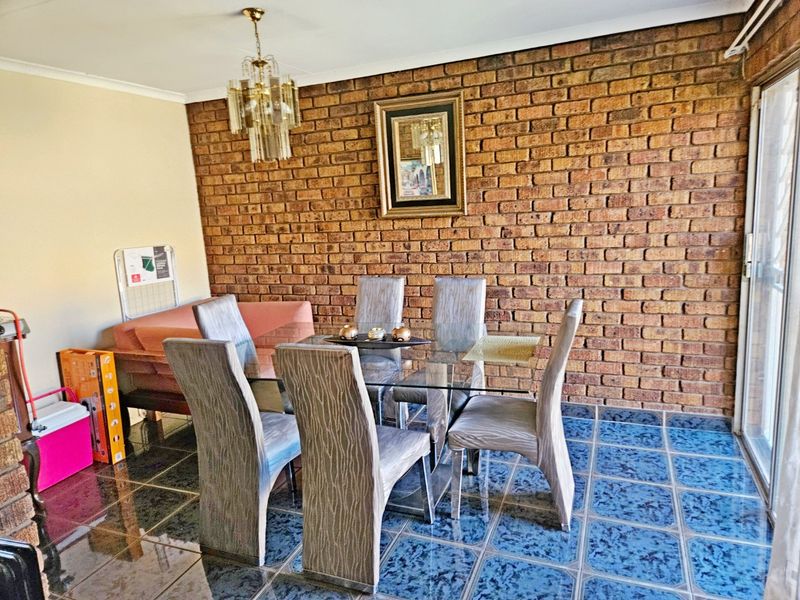 A dining area featuring a prominent exposed brick wall, polished blue ceramic floor tiles, and a sliding glass door providing natural light.