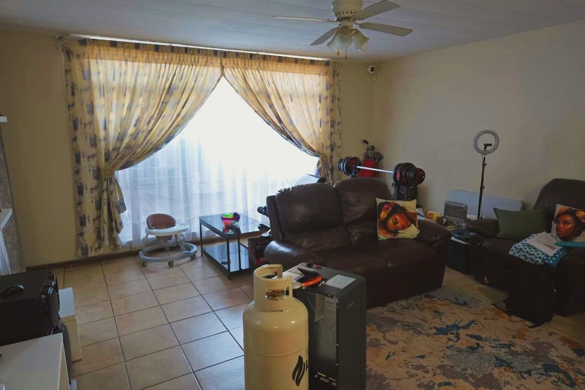 A living room featuring tiled flooring, a ceiling fan, and a large window providing natural light.
