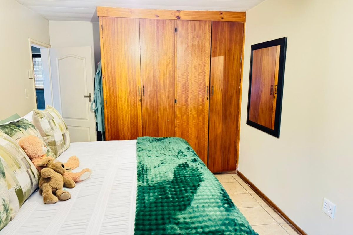 A bedroom featuring built-in wooden cupboards, tiled flooring, and a panelled ceiling, offering a functional space with classic finishes.
