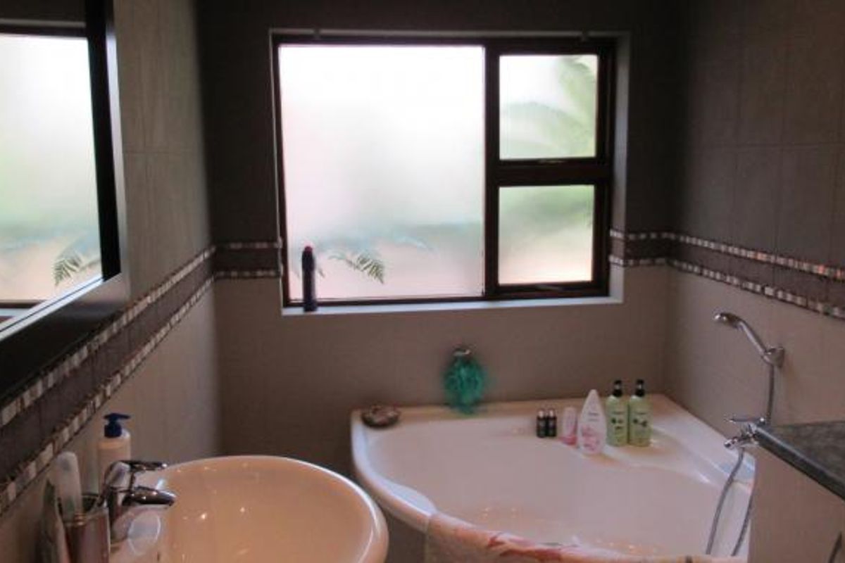 A modern bathroom featuring a corner bathtub, a vanity basin with a mirror, and tiled walls with decorative mosaic accents.