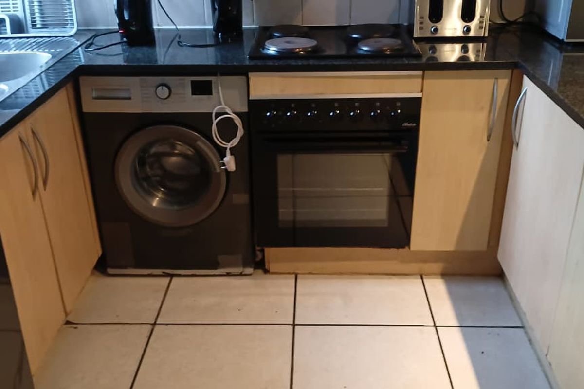 Compact kitchen featuring granite countertops, built-in oven, electric hob, and integrated cabinetry with tiled flooring.