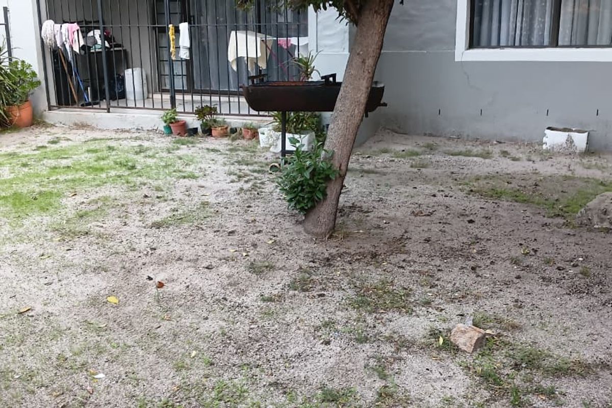 Rear exterior view of the apartment featuring a small garden area, security gate, and sliding door access.