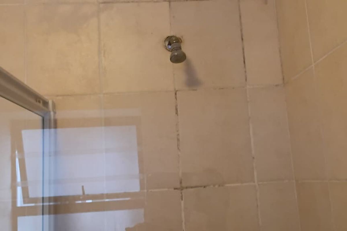 A bathroom shower enclosure featuring tiled walls and a glass screen, currently showing signs of wear and grout discoloration.