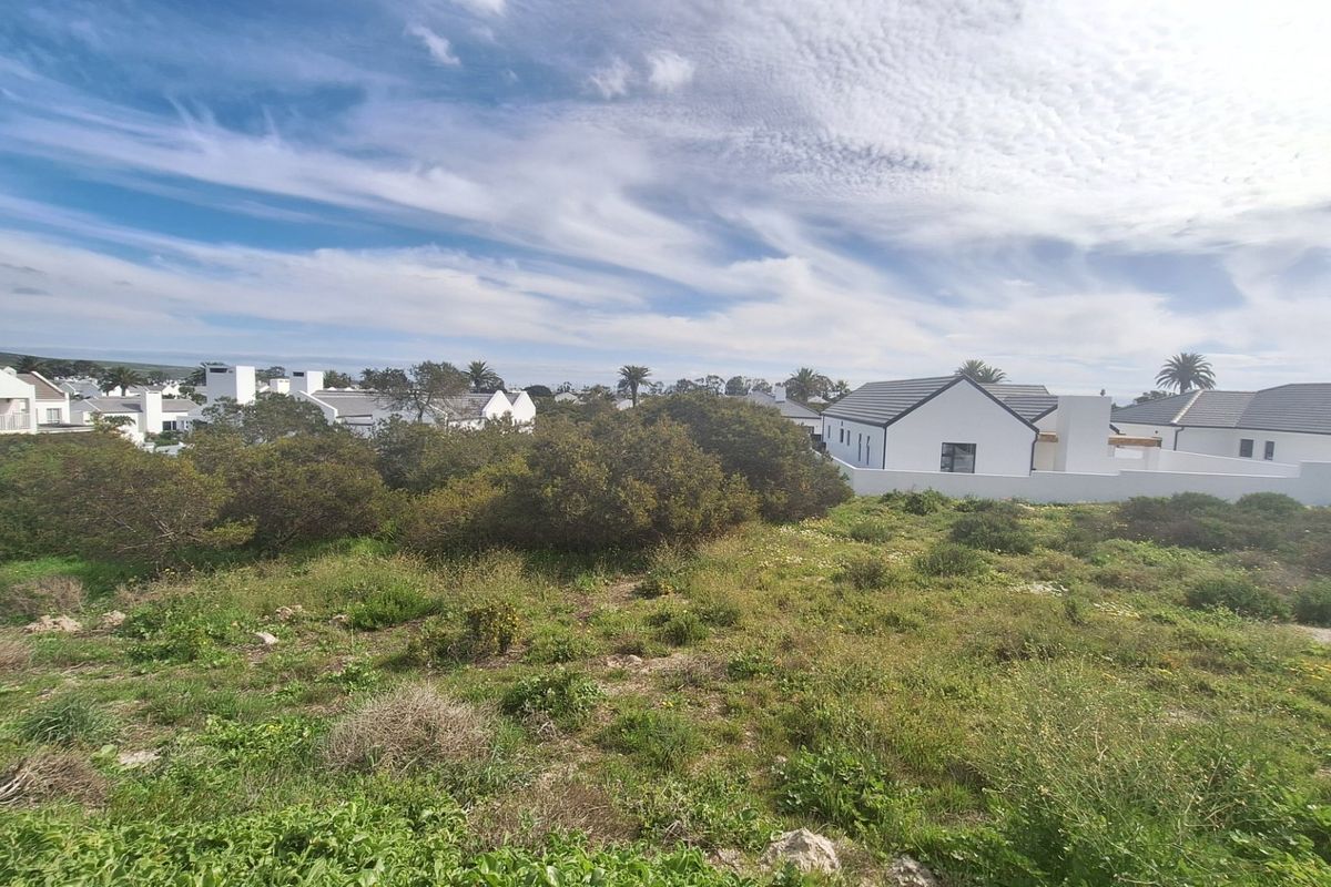 A view of a vacant residential plot featuring natural vegetation with established residential properties visible in the background.