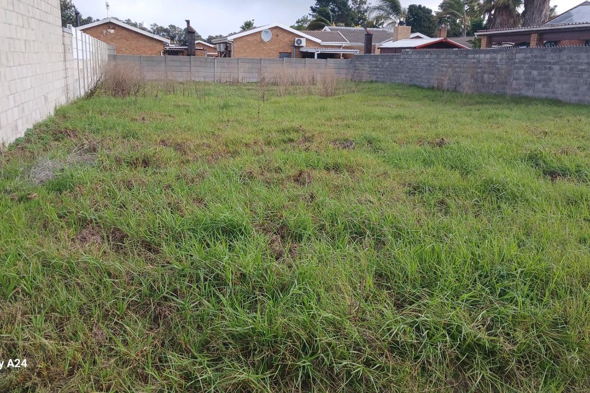 A vacant residential plot enclosed by perimeter concrete block walls, featuring overgrown grass and level ground suitable for development.