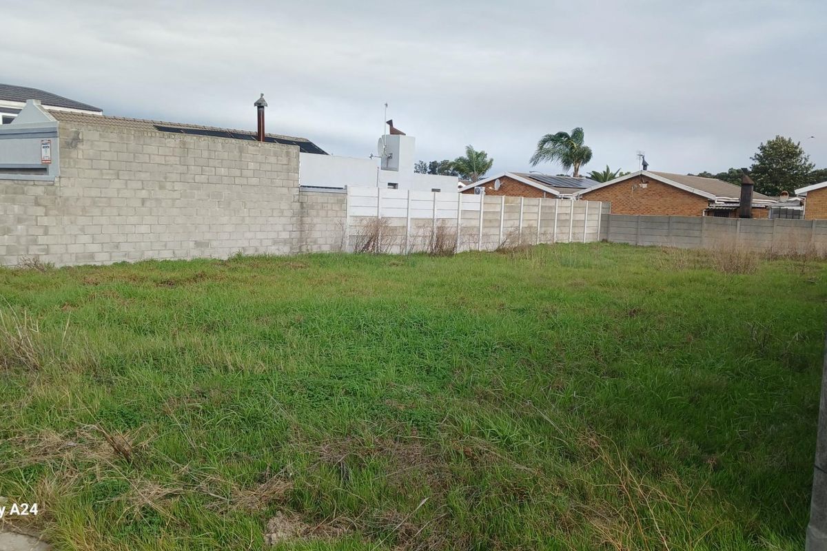 A vacant residential plot featuring grass coverage and enclosed by concrete block and precast boundary walls.