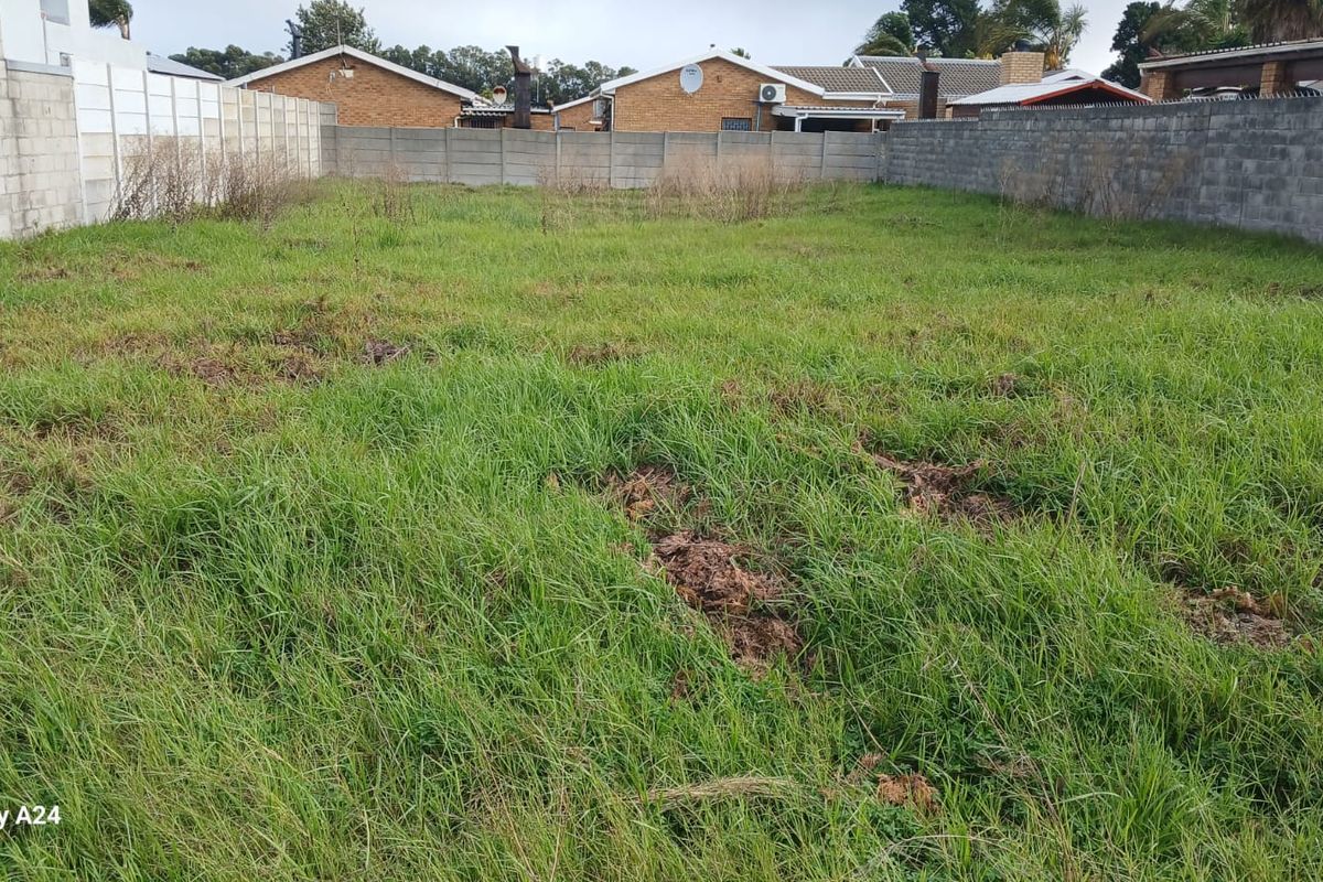 A vacant residential plot featuring a grass lawn enclosed by perimeter concrete block walls.