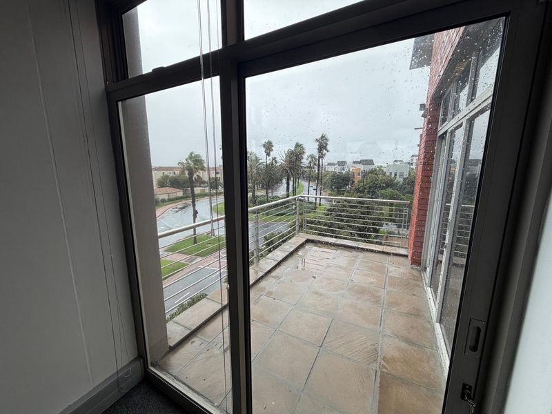 A covered balcony with tiled flooring and metal railings, offering an elevated view of the surrounding street and neighborhood.