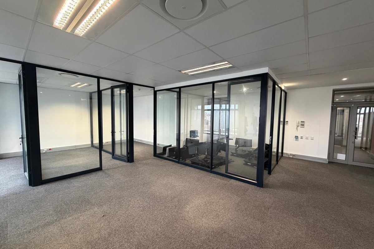 Modern commercial office space featuring glass-partitioned meeting rooms, suspended acoustic ceiling tiles, recessed fluorescent lighting, and neutral carpeting throughout.