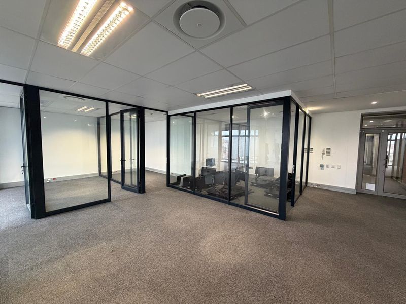 Modern commercial office space featuring glass-partitioned meeting rooms, suspended acoustic ceiling tiles, recessed fluorescent lighting, and neutral carpeting throughout.