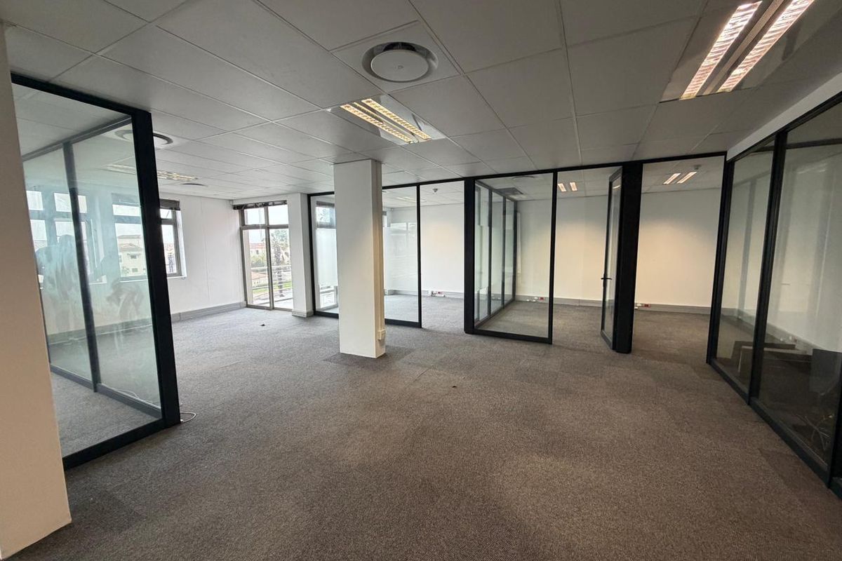 Open-plan commercial office space featuring glass partitioning, suspended ceiling tiles, recessed lighting, and carpeted flooring.