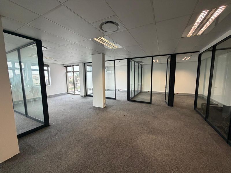 Open-plan commercial office space featuring glass partitioning, suspended ceiling tiles, recessed lighting, and carpeted flooring.
