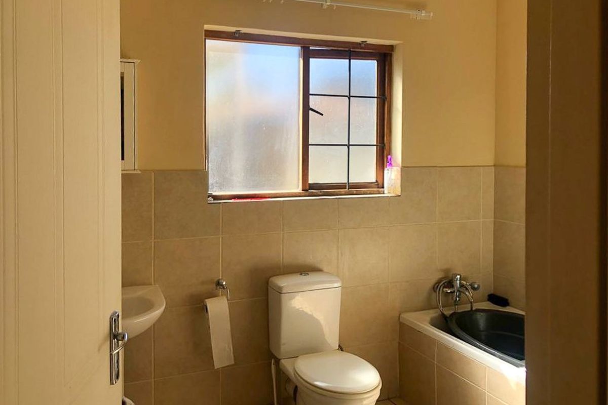 A functional bathroom featuring tiled walls and flooring, a built-in bathtub, a standard toilet, and a wall-mounted basin under a window.