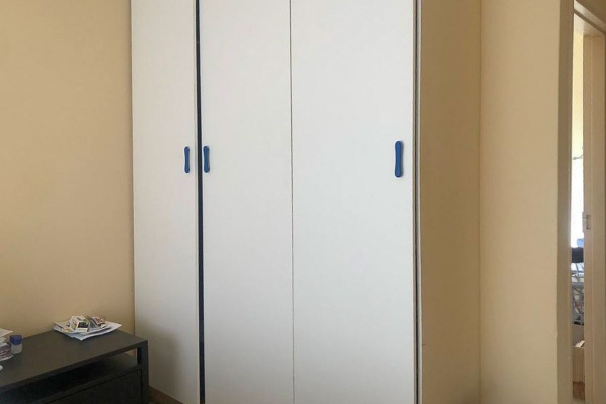 A bedroom featuring a white built-in wardrobe with blue handles, providing ample storage space.