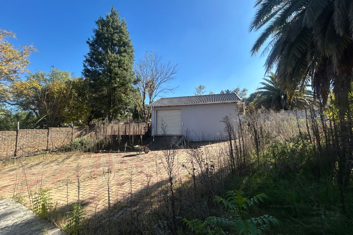 Rear exterior view featuring a detached garage, paved driveway, and extensive garden area requiring maintenance.