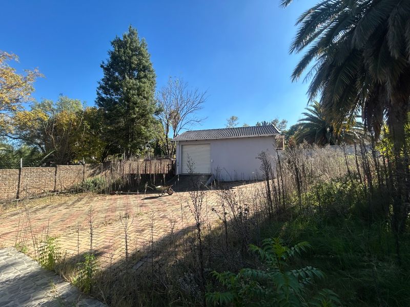 Rear exterior view featuring a detached garage, paved driveway, and extensive garden area requiring maintenance.
