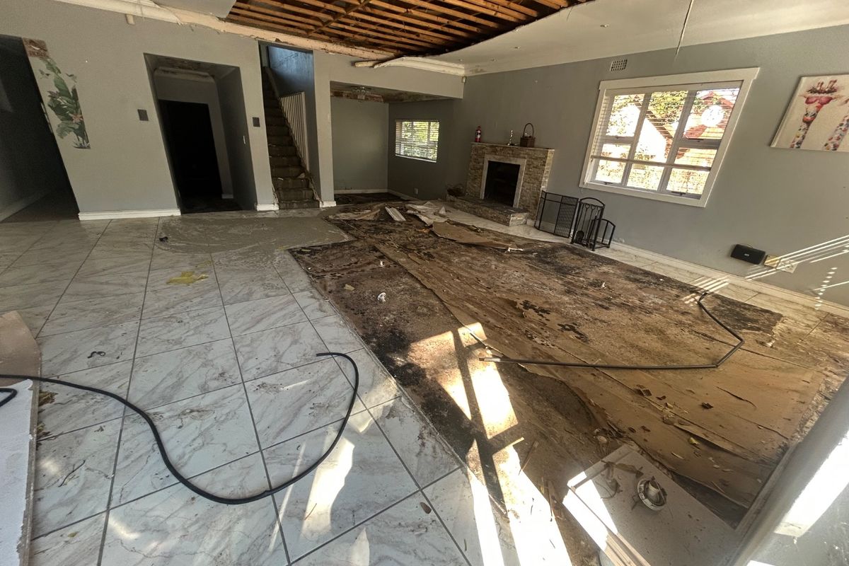 Spacious living area featuring a fireplace and staircase, currently undergoing significant renovation with exposed ceiling joists and damaged flooring requiring repair.