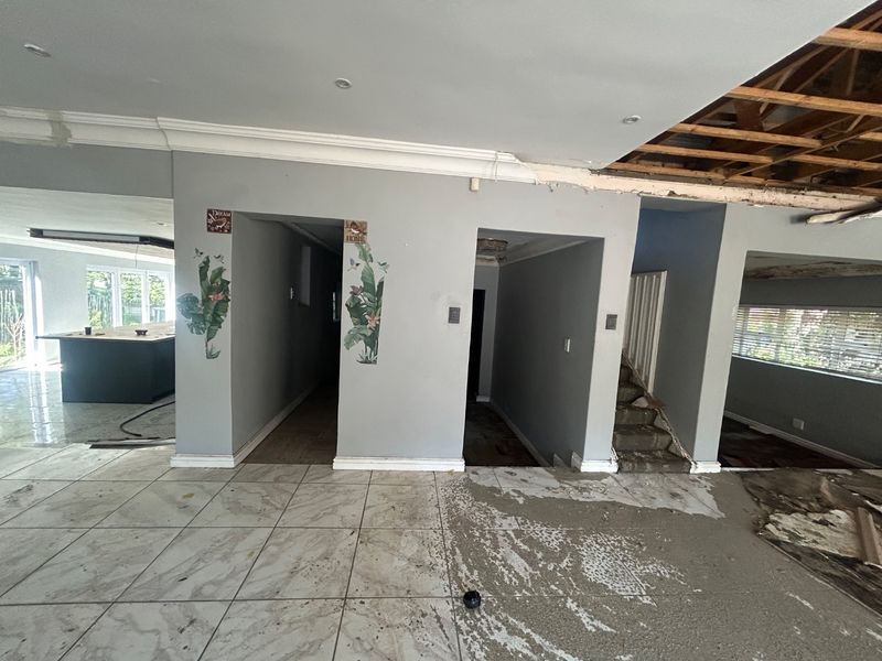 Open plan living area currently undergoing renovation, featuring exposed ceiling joists, tiled flooring, and a central staircase in need of completion.