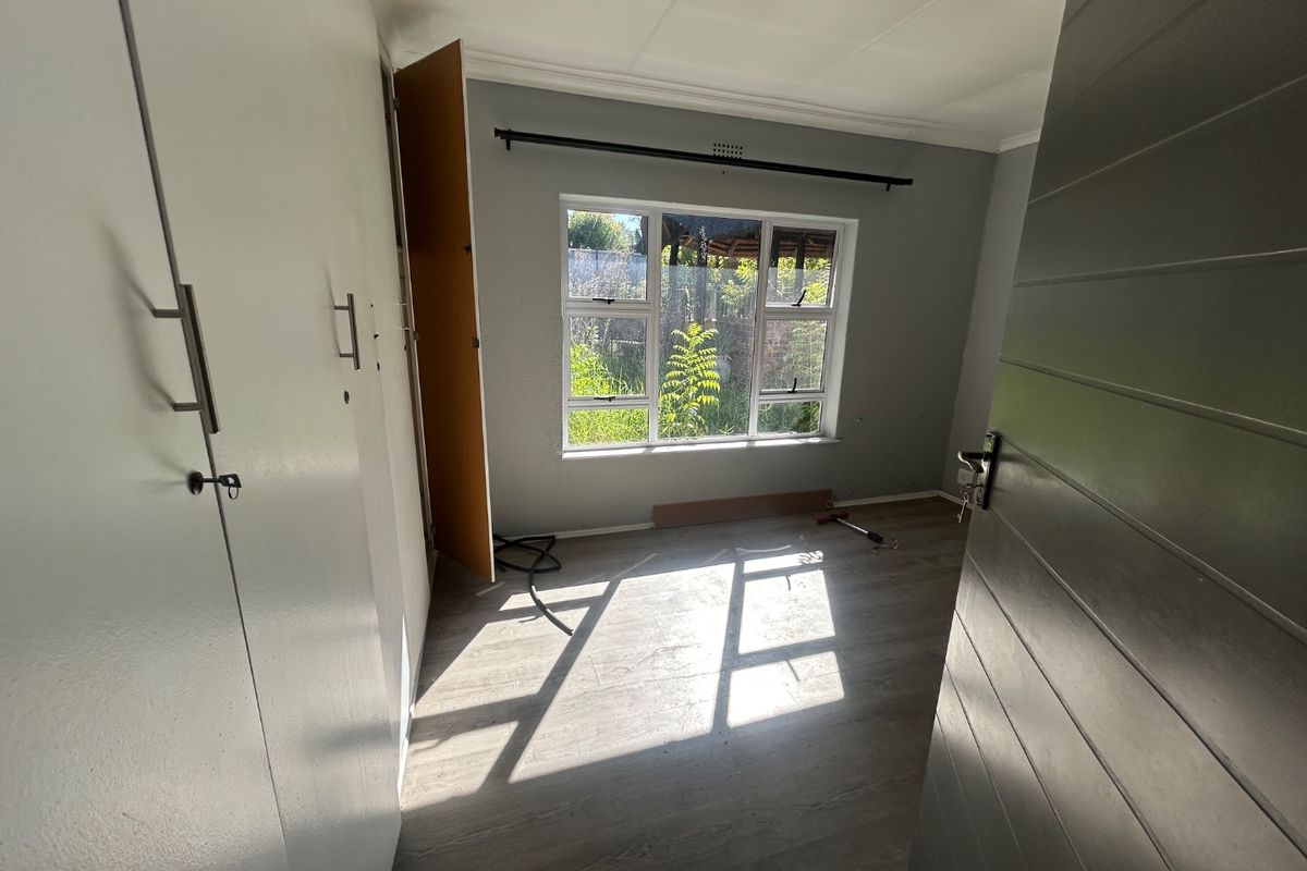 A bright, empty bedroom featuring modern laminate flooring, built-in cupboards, and large windows allowing for ample natural light.
