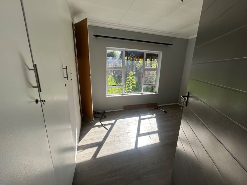 A bright, empty bedroom featuring modern laminate flooring, built-in cupboards, and large windows allowing for ample natural light.