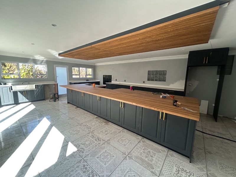 Spacious kitchen featuring a large island with wooden countertops, shaker-style cabinetry, and a unique suspended timber ceiling feature, currently in the final stages of completion.