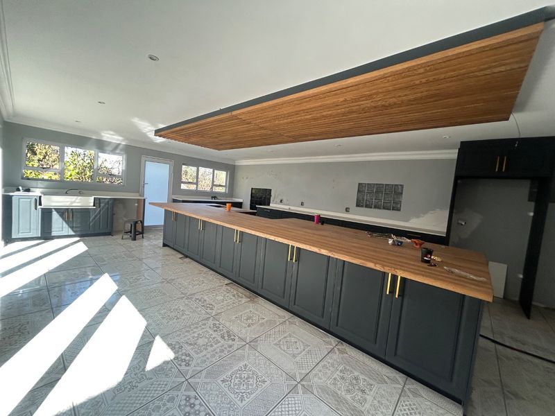 Spacious kitchen featuring a large island with wooden countertop, shaker cabinetry, and patterned floor tiles, currently undergoing final finishing touches.