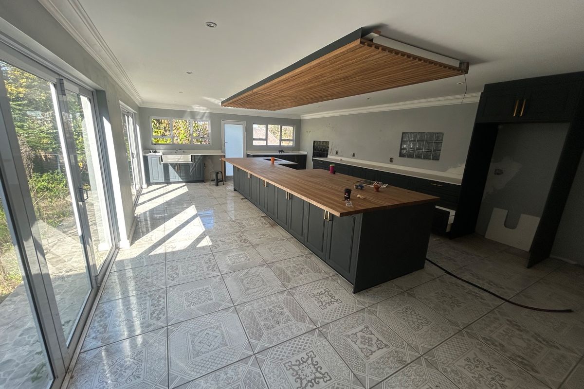 Spacious kitchen featuring a large island with wooden countertop, timber ceiling detail, and sliding glass doors leading to the exterior.