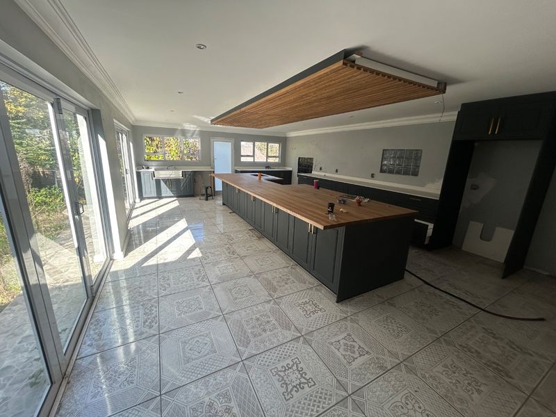 Spacious kitchen featuring a large island with wooden countertop, timber ceiling detail, and sliding glass doors leading to the exterior.