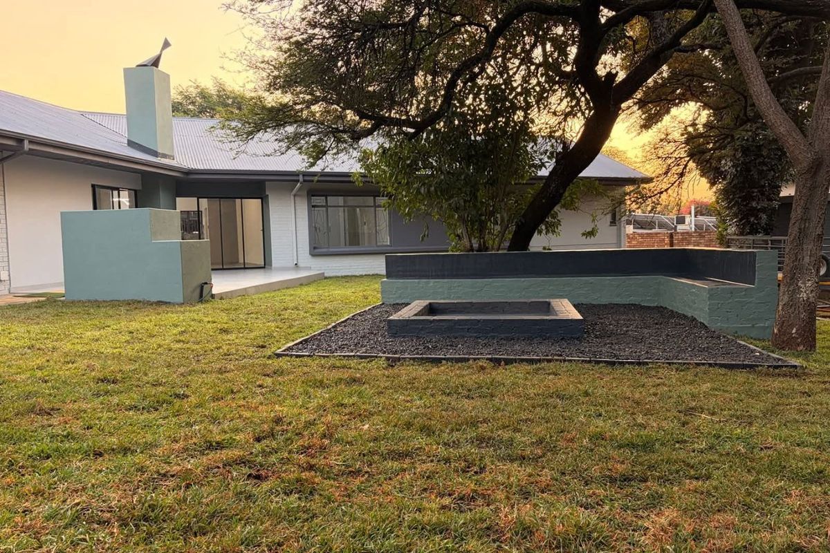 A well-maintained rear garden featuring a built-in fire pit with integrated bench seating, mature trees, and access to the home via sliding glass doors.