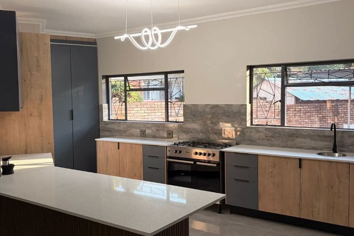 Modern kitchen featuring a large island, quartz countertops, two-tone cabinetry, gas stove, and sleek tiled flooring in a bright, open-plan layout.