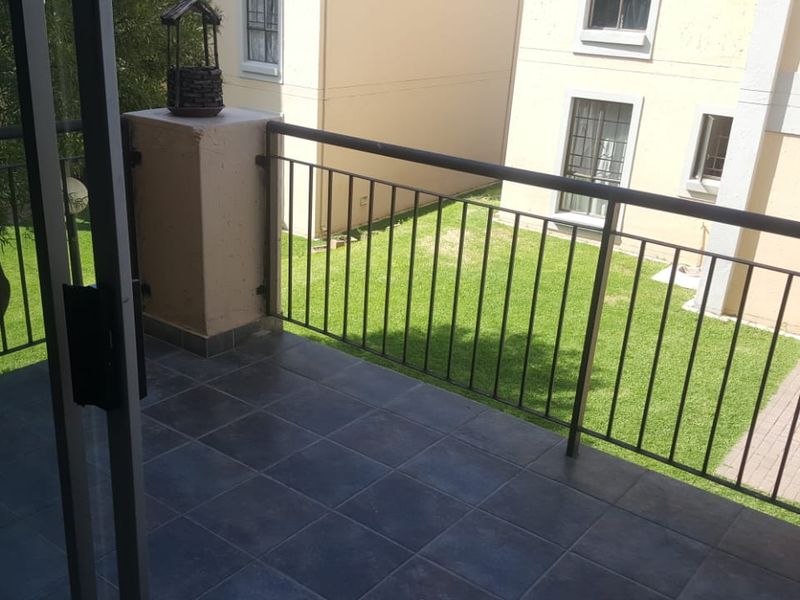 A private balcony featuring dark tiled flooring and a metal balustrade, overlooking a communal garden area.
