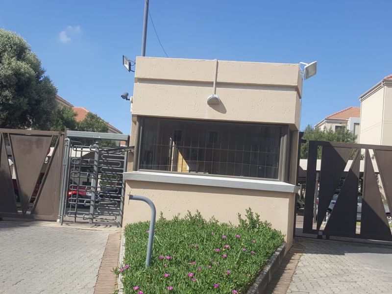 Secure apartment complex entrance featuring a guard house, automated vehicle gates, and a pedestrian turnstile for controlled access.